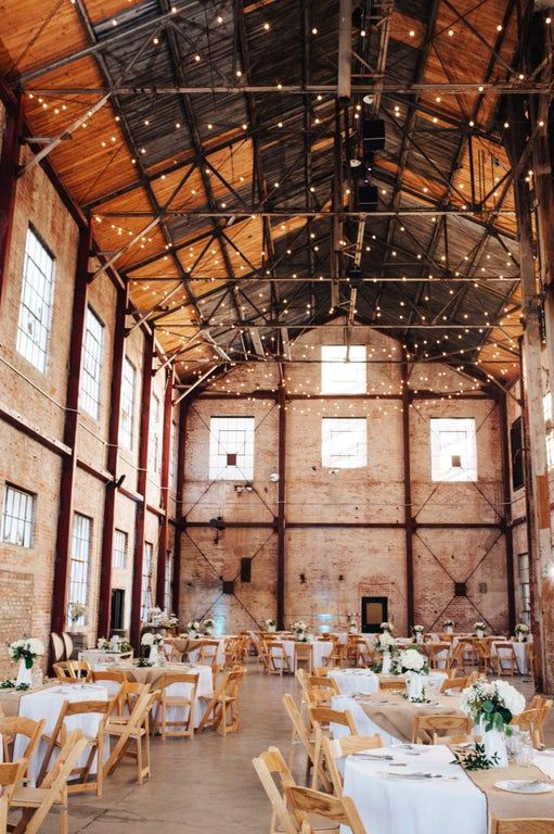 an industrial wedding reception space with wooden shutters, metal beams, lights and brick walls plus elegant tablescapes