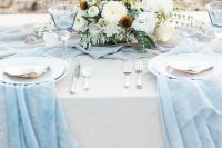 an oceanside wedding tablescape with serenity blue runners, white plates and large seashells, white blooms