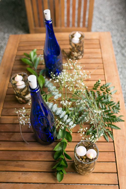 beautiful wedding decor with greenery, white blooms, floating candles in glasses and usual candles in bright blue wine bottles