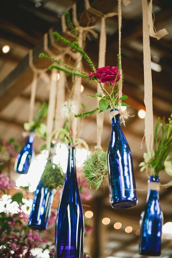 blue wine bottles with greenery and blooms hanging on burlap are lovely decorations for a rustic or woodland wedding
