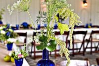 bright blue wine bottles wrapped with burlap and twine, blue vases and glasses with blooms and greenery and blue candleholders to style a rustic wedding