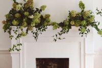 candles in glass candleholders, greenery and green hydrangeas make the fireplace stand out contrasting to the greens