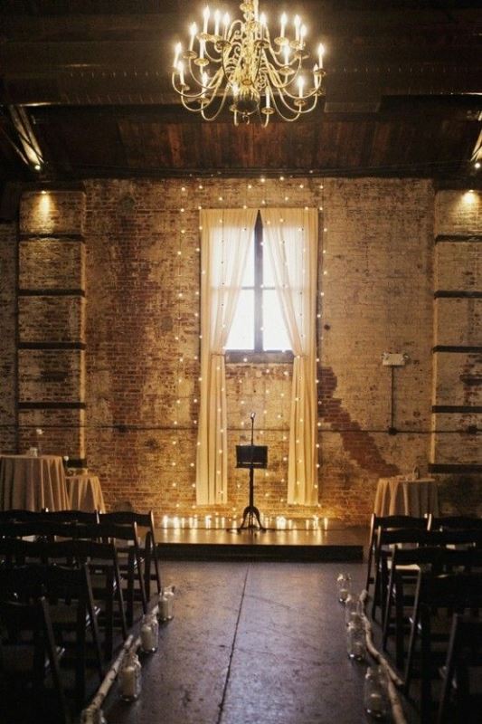a dark industrial wedding space with shabby brick walls, lights and curtains, candles to decorate the altar and line up the aisle