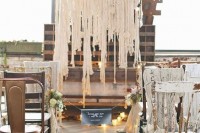 a shabby industrial wedding space with a macrame and lights backdrop, shabby chairs, blooms and a chalkboard sign