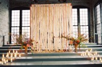 a wedding ceremony space with colorful fabric ribbons, bright blooms in vases and candles to line up the altar