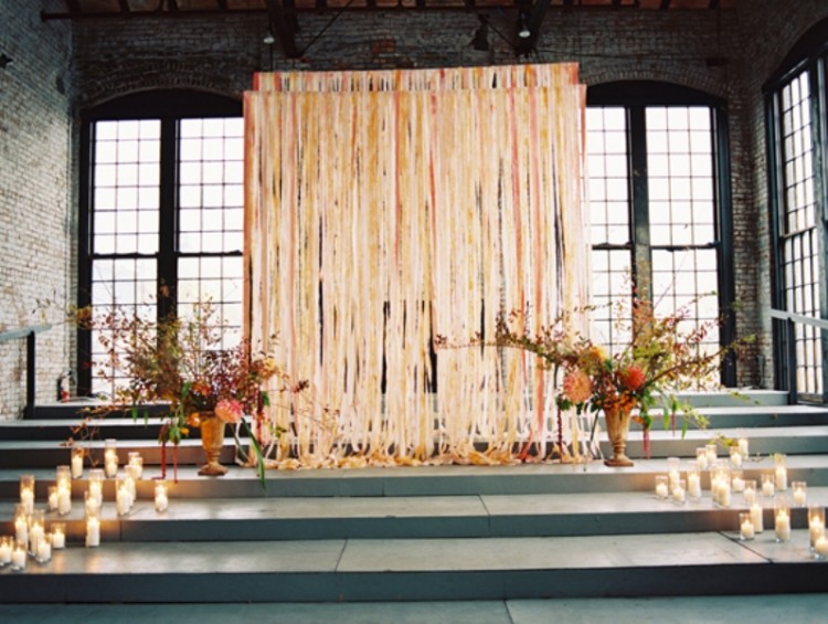 a wedding ceremony space with colorful fabric ribbons, bright blooms in vases and candles to line up the altar