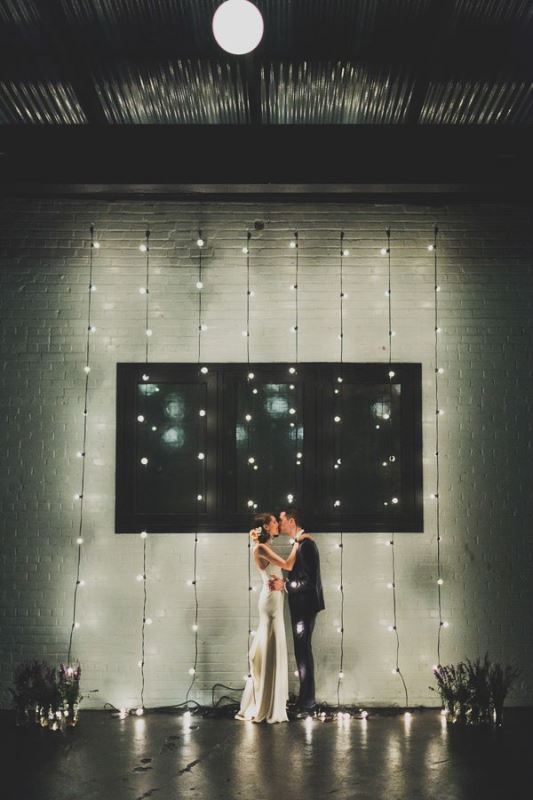 a wedding ceremony space with white brick walls, lights, dried bloom arrangements for a simple and stylish modern look