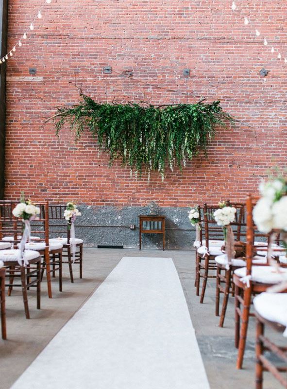 an industrial wedding cermeony space with a lush greenery decoration and white blooms and ribbon bows to soften the space