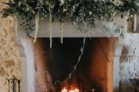 pillar candles in the fireplace and a lush greenery and white bloom decoration on the mantel make the fireplace super cool