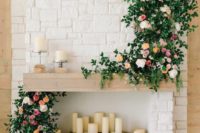 pillar candles, lush greenery and pink blooms make the fireplace chic and very beautiful, a perfect wedding backdrop