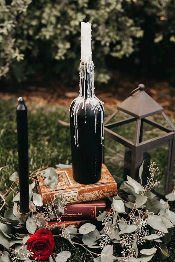 refined Halloween wedding decor with a black wine bottle with a candle, a black candle, some books, eucalyptus and a candle lantern