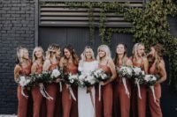 rust-colored bridesmaid jumpsuits with square cuts and cropped pants, white mules and white bouquets for a boho wedding