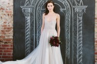 an A-line off-white wedding dress with an embellished bodice, a deep neckline, no sleeves and a layered skirt with a train