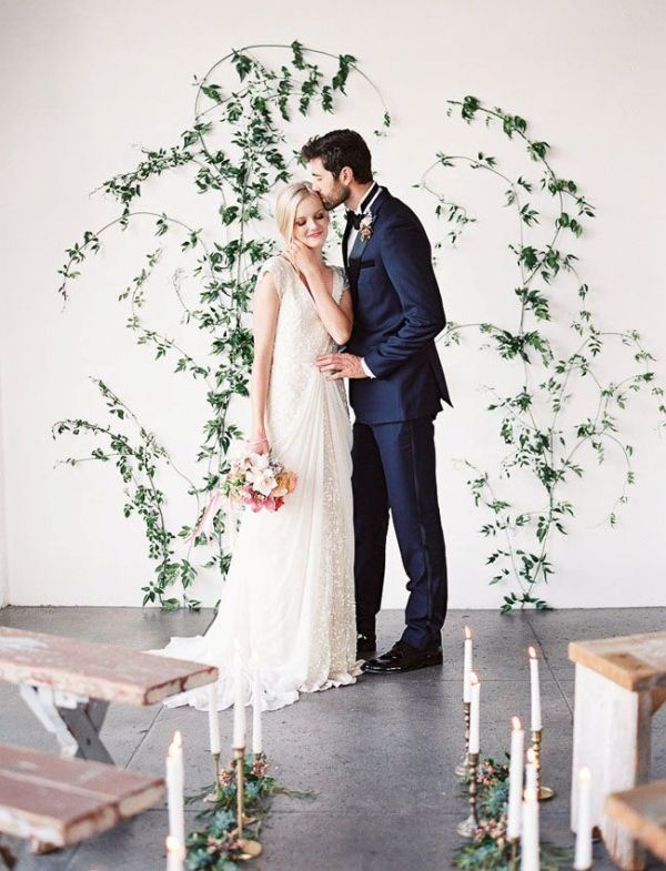 an ethereal and chic greeenery wedding backdrop indoors - some greenery branches attached right to the wall and greenery lining up the aisle