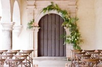 a vintage door with greenery and white blooms and candles, ferns and grey candles to line up the aisle for a romantic feel