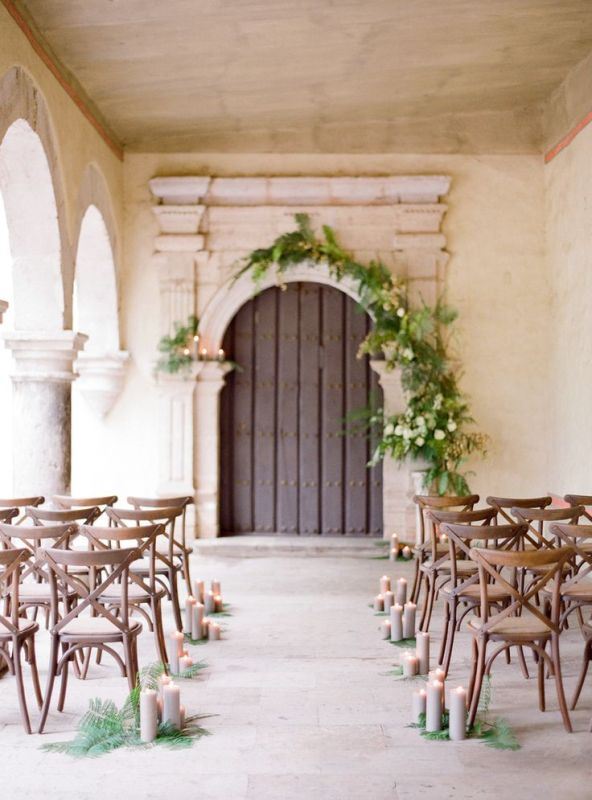 a vintage door with greenery and white blooms and candles, ferns and grey candles to line up the aisle for a romantic feel
