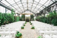 a lush greenery wedding space with foliage and greenery and white blooms hanging down, greenery and petals to line up the aisle