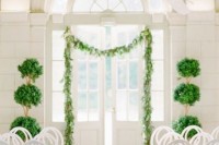 a refined romantic wedding ceremony space with a greenery garland attached to the doorway, greenery topiaries and greenery garlands on the chair