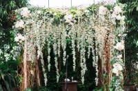 a lovely botanical wedding backdrop – a lush greenery and white bloom arch with floating candles and some lanterns to line up the aisle