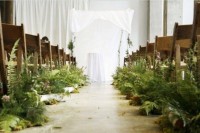 a botanical wedding ceremony space with white textiles and lush ferns lining up the aisle to make it look woodland-like