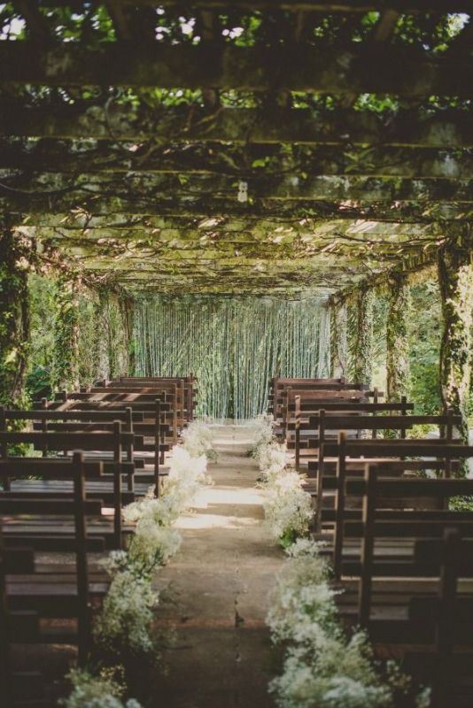 a lush botanical wedding ceremony space with greenery all over the space and baby's breath lining up the aisle