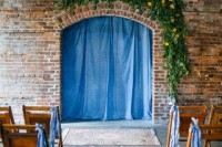 a blue denim backdrop paired with greenery and yellow blooms and denim ribbons on the chairs for a casual or industrial wedding