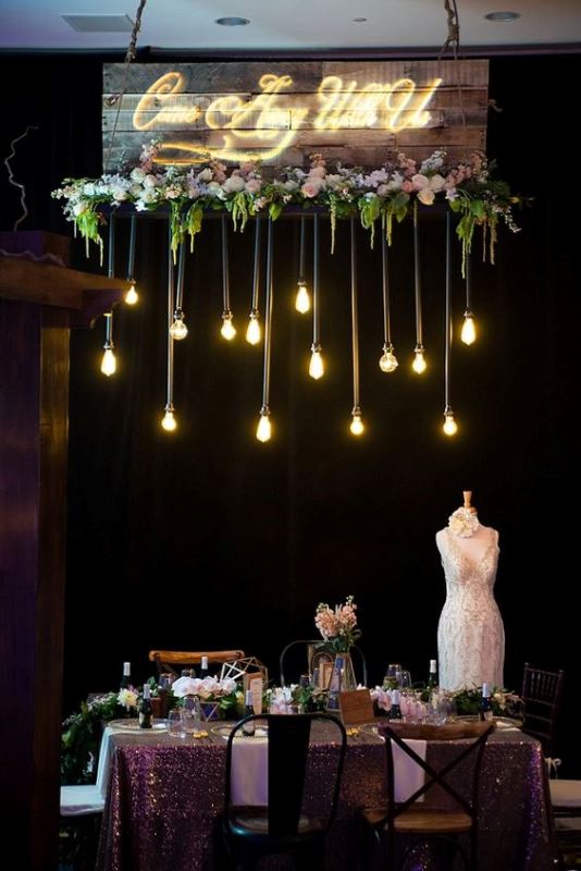 a refined wedding reception space with a pink sequin tablecloth, candles, blooms and bulbs over the table for a catchier look