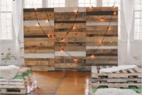 a rustic wedding ceremony space with a reclaimed wood wall, bulbs on it, pallet and faux fur benches and candles