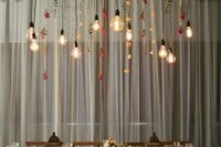 a bold wedding reception space with a wooden table, neutral blooms and an overhead installation with hanging blooms and bulbs is very elegant and rather cozy