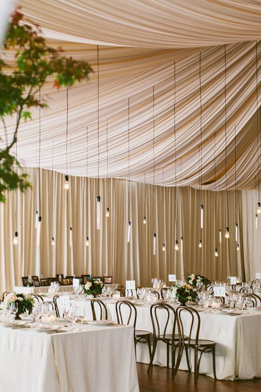 an elegant neutral wedding tent with bulbs hanging down is a lovely idea, they accent the tent and give enough light to the space