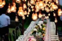 an outdoor wedding reception with lots of blooms, candles and hanging bulbs over the table to make the reception space cozier and more welcoming