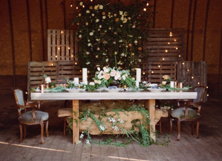 a reception space decorated with wooden screens with lights, greenery and neutral blooms, greenery runners and a decoration under the table