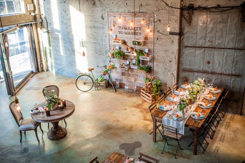 an industrial reception space with shabby walls, bulbs, and greenery and bright blooms that enliven and soften the decor