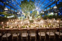an eye-catchy and charming wedding reception with potted greenery and trees, greenery chandeliers with lights and greenery and bloom runners