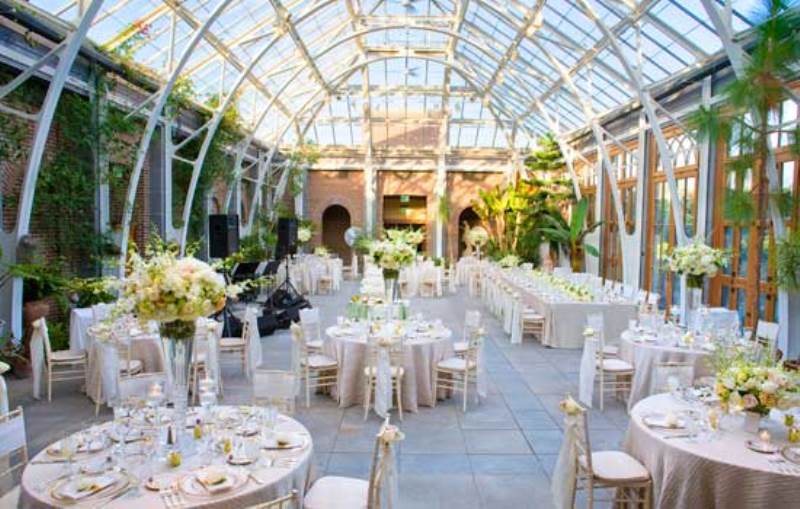 an elegant and refined wedding venue with greenery climbing up the walls, neutral and pastel blooms for centerpieces