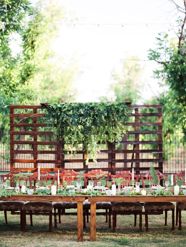 a backyard wedding reception with a wooden screen and greeenery, greenery runners and ferns and candles looks chic