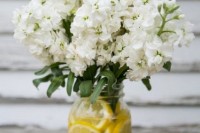 a bright wedding centerpiece of a jar with lemon slices and white blooms is a gorgeous idea for a summer wedding