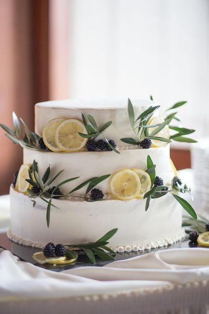 a white buttercream wedding cake with lemon slices, herbs and blackberries is a lovely summer or fall wedding cake