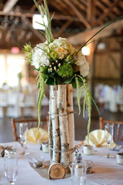 a rustic wedding centerpiece of birch branches, white blooms and greenery plus a wood slice is a gorgeous idea for a rustic wedding