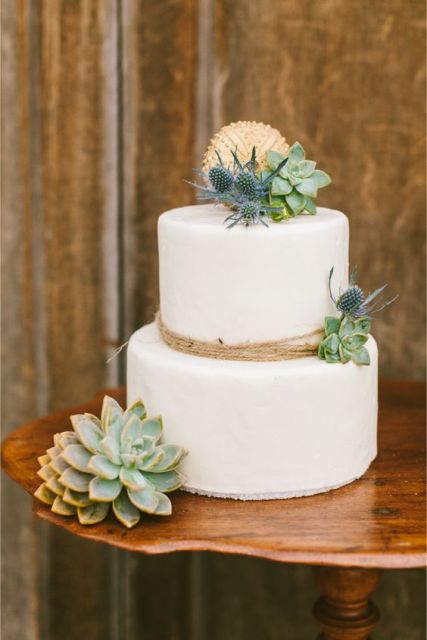 a white wedding cake decorated with twine, with succulents, thistles and with a large ball on top for a rustic coastal wedding