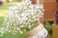an aisle decoration of a jar with lace and twine and baby’s breath is a stylish idea for a rustic wedding