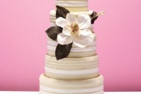 a striped wedding cake decorated with a large magnolia bloom and dark leaves is a cool idea for a chic wedding