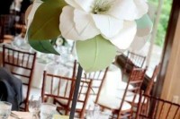 a tall wedding centerpiece of a single magnolia with leaves is a cool idea to decorate a tablescape and make a statement