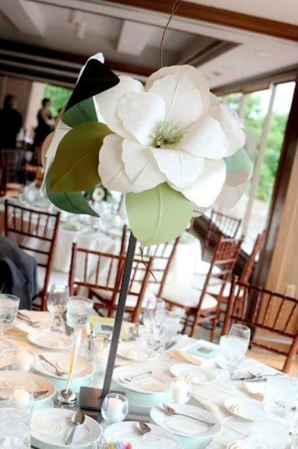 a tall wedding centerpiece of a single magnolia with leaves is a cool idea to decorate a tablescape and make a statement