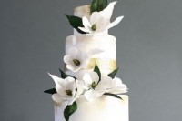 a white wedding cake with gold ribbons and white magnolias is a chic and glam idea for a modern wedding