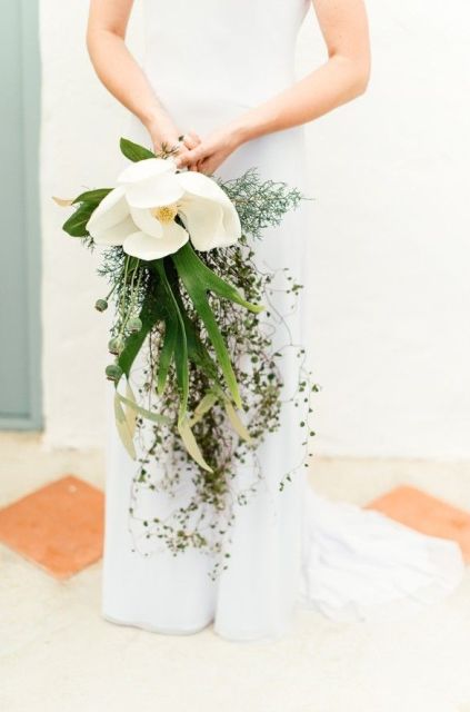 a cascading wedding bouquet of greenery and large magnolias is a creative and chic idea