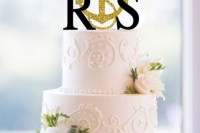 a white textural wedding cake decorated with neutral blooms, monograms and a gold glitter anchor topper is a stylish idea for a wedding