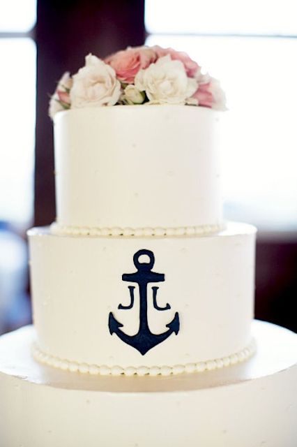 a white wedding cake decorated with pink and white blooms and a black anchor is a bold and cool idea for a nautical wedding or a seaside one