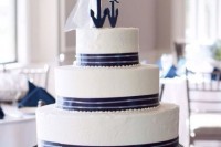a white wedding cake with navy ribbons, navy anchor cake toppers is a stylish idea for a nautical wedding