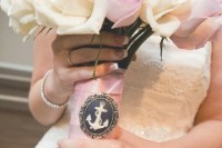 a neutral wedding bouquet with neutral and blush roses, decorated with a pink wrap and an anchor pendant is a lovely idea for a nautical wedding